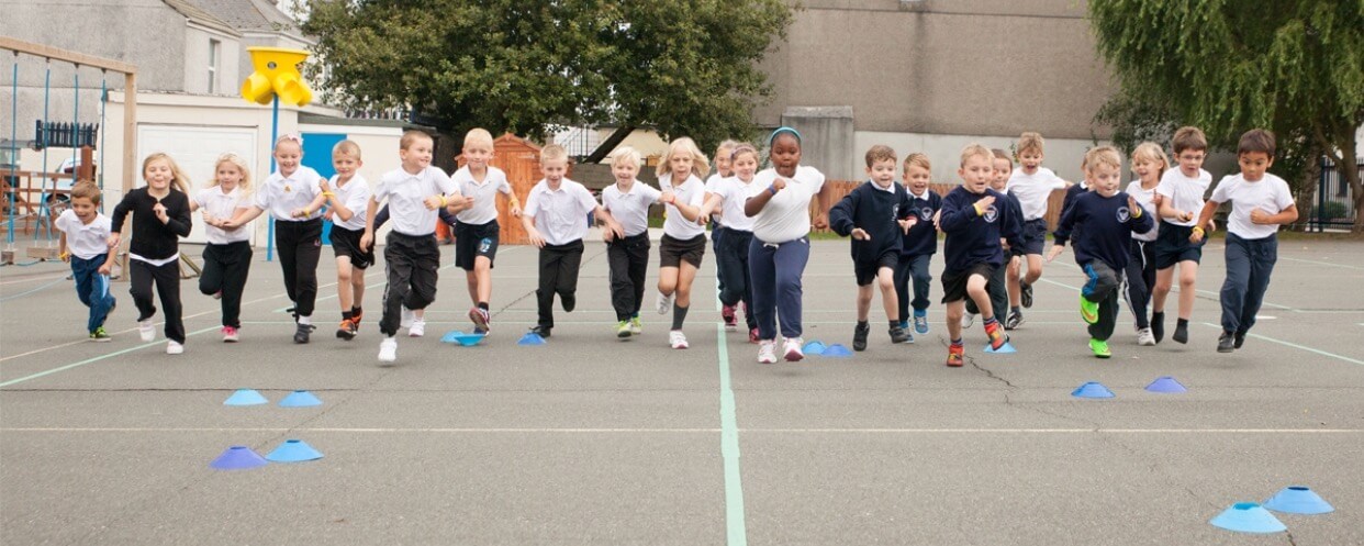 Children running across playground during PE Sports Education at a primary school